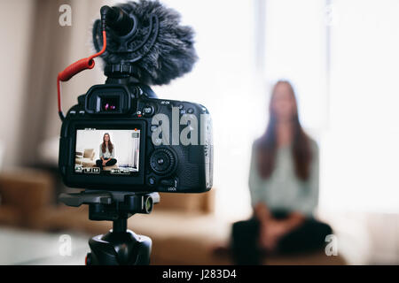 Junge weibliche Vloggerin Videoaufnahme sitzen in ihrem Wohnzimmer. Kamerabildschirm zeigt die live-Aufnahme von video-Blog. Stockfoto