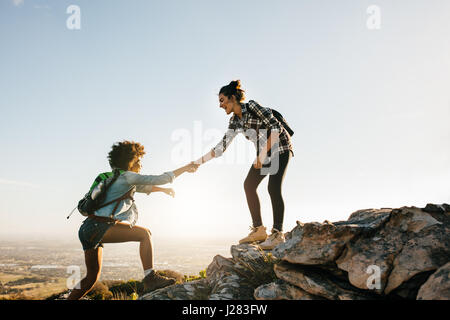 Junge Frau hilft Freund zu dem Felsen erklimmen. Zwei junge Frauen, die in der Natur wandern. Stockfoto