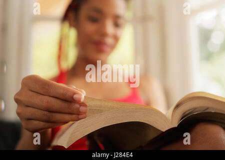 Glückliche Studentin Buch zu lesen und auf Sofa sitzen. Junge afrikanische amerikanische Frau, entspannend, schwarze Mädchen auf der Couch liegen. Hispanische People- und lifestyle Stockfoto