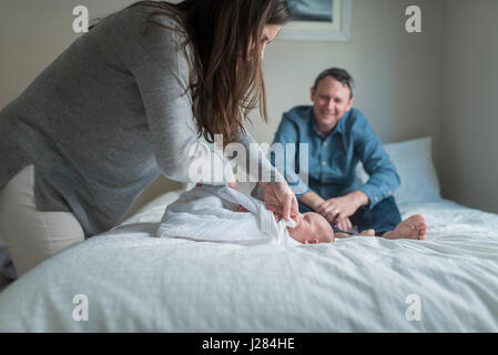 Seitenansicht der Mutter Windeln neugeborenes Baby Boy mit Decke während Vater im Hintergrund Stockfoto