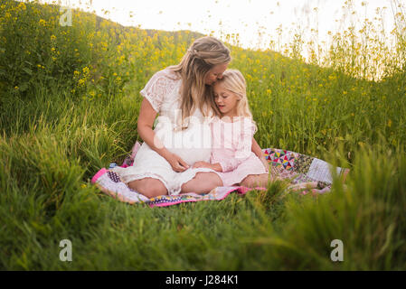 Glückliche Mutter Tochter auf Stirn küssen, während Sie sitzen im park Stockfoto