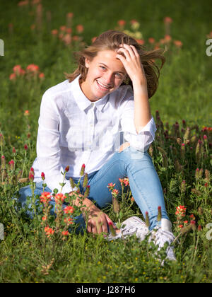 Junge Frau sitzt im Bett von wilden Blumen Stockfoto