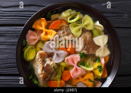 Italienische Suppe mit Schweinefleisch, farbige Farfalle Nudeln und Gemüse in eine Schüssel Nahaufnahme. horizontale Ansicht von oben Stockfoto