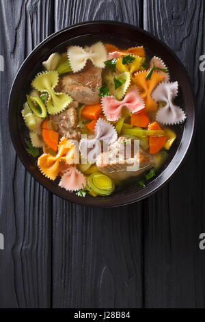 Köstliche Suppe mit Fleisch, bunten Farfalle Nudeln und Gemüse in eine Schüssel Nahaufnahme. Vertikale Ansicht von oben Stockfoto