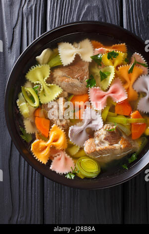 Italienische Suppe mit Schweinefleisch, farbige Farfalle Nudeln und Gemüse in eine Schüssel Nahaufnahme. Vertikale Ansicht von oben Stockfoto