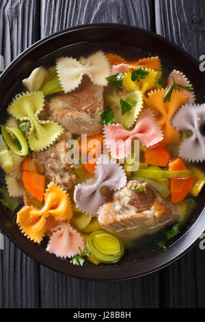 Deftige Fleischsuppe mit farbigen Farfalle Nudeln und Gemüse in eine Schüssel Nahaufnahme. Vertikale Ansicht von oben Stockfoto