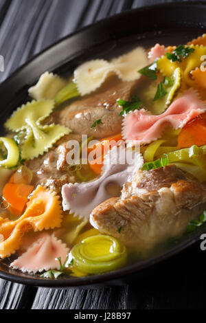 Italienische Fleischsuppe mit farbigen Farfalle Nudeln und Gemüse in eine Schüssel Nahaufnahme. vertikale Stockfoto