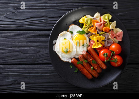 herzhaftes Frühstück: gebratenen Eiern, Würstchen, Farfalle Pasta und Tomaten Nahaufnahme auf einer Platte. Horizontale Ansicht von oben Stockfoto