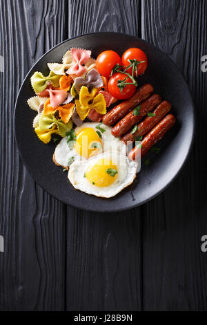 herzhaftes Frühstück: gebratenen Eiern, Würstchen, Farfalle Pasta und Tomaten Nahaufnahme auf einer Platte. Vertikale Ansicht von oben Stockfoto