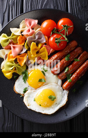 Spiegelei, Würstchen, Nudeln Farfalle und Tomate Nahaufnahme auf einer Platte. Vertikale Ansicht von oben Stockfoto