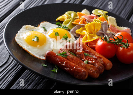 Spiegeleier mit Würstchen, farbige Farfalle Pasta und Tomaten Closeup auf einem Teller. horizontale Stockfoto