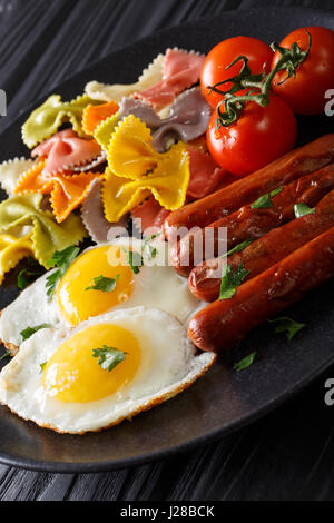 herzhaftes Frühstück: gebratenen Eiern, Würstchen, Farfalle Pasta und Tomaten Nahaufnahme auf einer Platte. vertikale Stockfoto