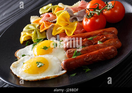 Spiegelei, Würstchen, Nudeln Farfalle und Tomate Nahaufnahme auf einer Platte. Horizontale Stockfoto
