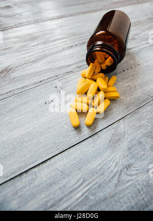 Gelbe Pillen auf Holztisch verschüttet. Getönten Foto, geringe Schärfentiefe. Stockfoto