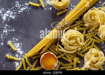 Verschiedene Arten von Pasta Spaghetti, Fusilli, Fettuccine und rohes Eigelb auf einem Küchentisch aus Holz. Kopieren Sie Raum. Stockfoto