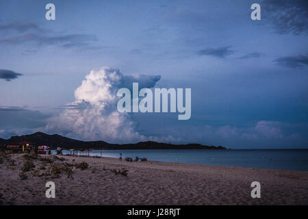 Leeren Strand in der Abenddämmerung in Costa Rei, Sardinien, Italien. Dramatische Wolken in der blauen Stunde, die aussehen wie eine Form eines riesigen Hundes. Berge im Hintergrund Stockfoto