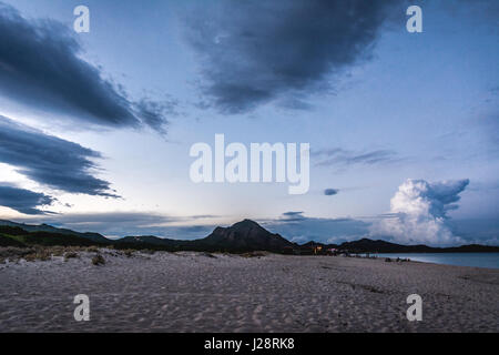 Leeren Strand in der Abenddämmerung in Costa Rei, Sardinien, Italien. Dramatische Wolken in der blauen Stunde, die aussehen wie eine Form eines riesigen Hundes. Berge im Hintergrund Stockfoto