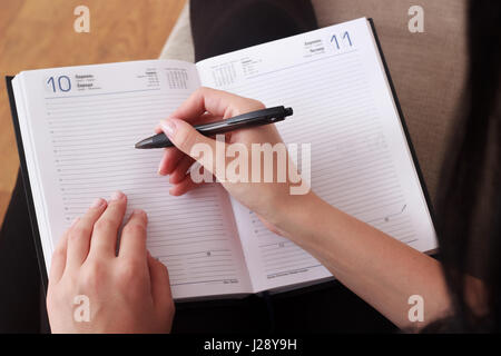 Hand ist in einem Notizbuch auf einem Holztisch schreiben. Stockfoto