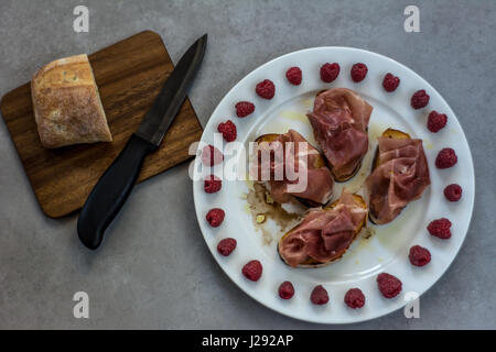 Tapas Jamon Serrano oder italienischen Schinken und Brot auf einem Holzbrett. Dekoriert mit Himbeeren. Ansicht von oben. Stockfoto