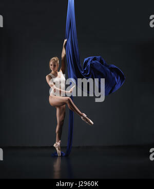 Schlanke Blondine in beigen Bodysuit auf blauen aerial Silk Stockfoto