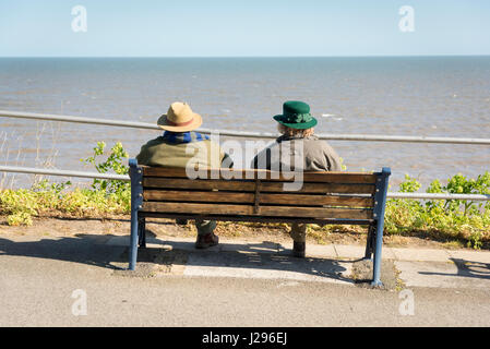 Ansicht von hinten von zwei Personen in Hüte und Mäntel bei sonnigem Wetter sitzt auf einer Sitzbank mit Blick auf das Meer bei Cromer Norfolk UK Stockfoto