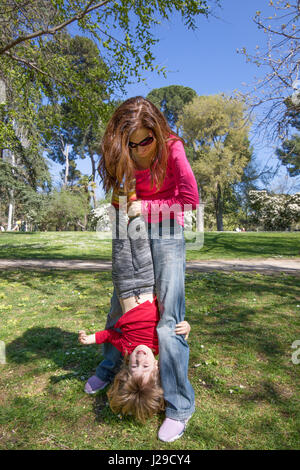 drei Jahre alte blonde Kind lachendes Gesicht, Hände kopfüber hängen von der Frau Mutter, spielen auf der grünen Wiese im öffentlichen park Stockfoto
