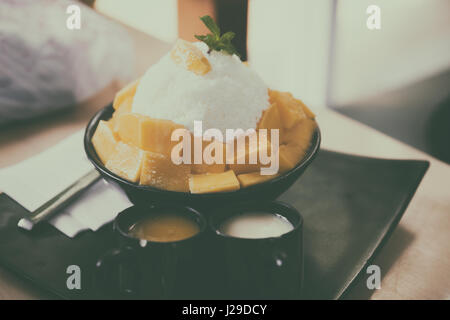 Rasiert Eis mit frischer Mango Dessert auf schwarze Platte serviert mit Mango-Sirup Stockfoto