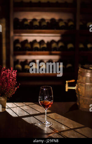 Weinglas platziert neben den Lauf und Blume Weintopf auf einem Holztisch in einem Weinkeller. Stockfoto