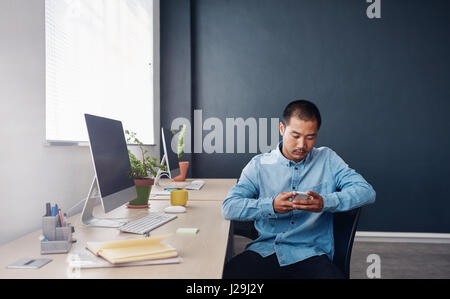 Junge asiatische Designer sitzen in einem Büro, SMS-Nachrichten lesen Stockfoto