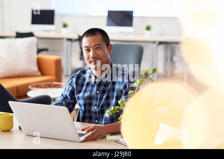 Junge asiatische Designer arbeitet auf einem Laptop in einem Büro Stockfoto