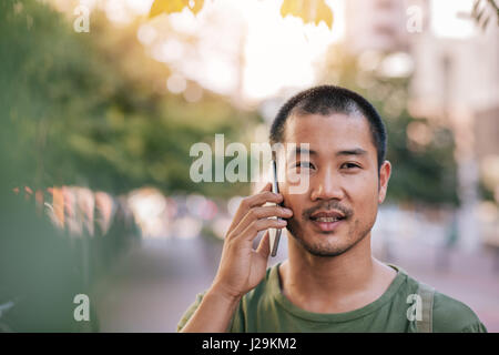 Junge asiatische Mann reden auf seinem Handy außerhalb Stockfoto