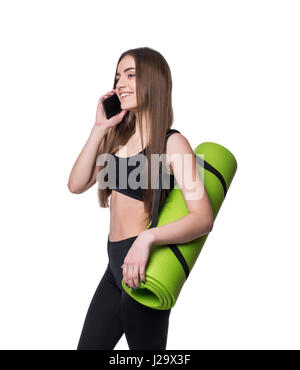 Süße junge Frau in Sportkleidung mit grünen Matte bereit für Training. Lächeln auf den Lippen und am Telefon zu sprechen. Isoliert auf weißem Hintergrund Stockfoto