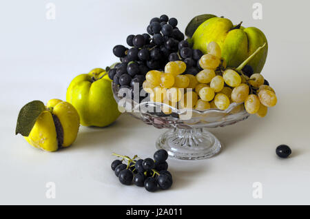 Sortierte Herbstfrüchte - Trauben, Quitte - in einer kleinen Kristall-Vase auf einem weißen Hintergrund isoliert Stockfoto
