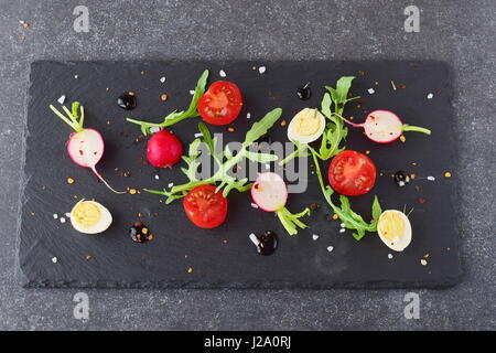 Frische Radieschen, Kirschtomaten, Wachtelei, Parmeggiano mit Balsamico-Glasur auf einem schwarzen Steinplatte. Mediterranes Lebensgefühl. Gesunde Ernährung. Stockfoto