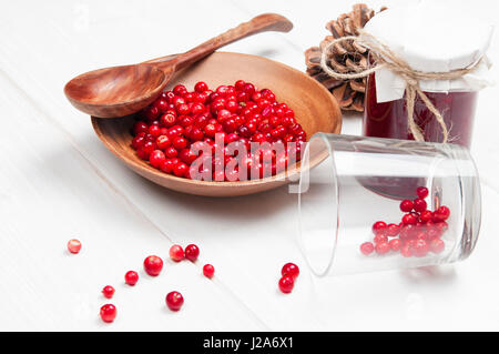 Preiselbeeren in Holzschale mit Löffel und Marmelade im Glas auf weißem Untergrund Stockfoto