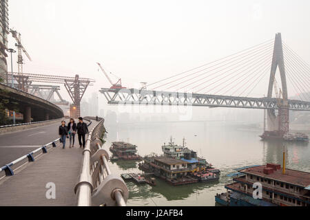 China, Chongqing, Fußgänger zu Fuß entlang der Brücke mit Blick auf Bau von massiven Dongshuimen Brückenneubau in der Abenddämmerung entlang Yangtze-Fluss an trüben Herbstabend Stockfoto