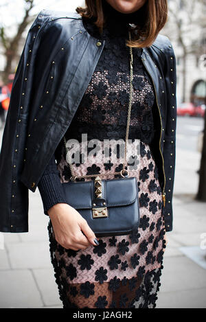 LONDON - Februar 2017: Mittelteil der modebewussten Frau trägt eine schwarzes Spitzenkleid mit Lederjacke über ihre Schultern und ein Valentino überqueren Sie Körper Handtasche, London Fashion Week, vertikale, front Ansicht Stockfoto