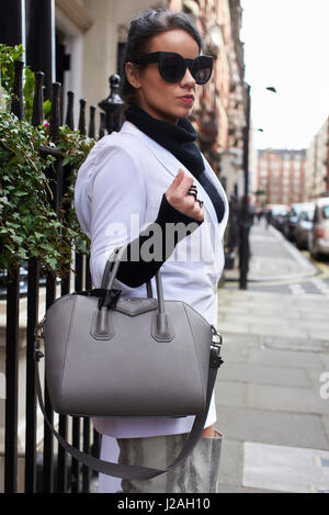 LONDON - Februar 2017: Drei Viertel Länge sehen Frau in Sonnenbrille auf Straße halten Designer-Handtasche Pringle of Scotland Show, London Fashion Week, Tag vier draußen stehen. Stockfoto