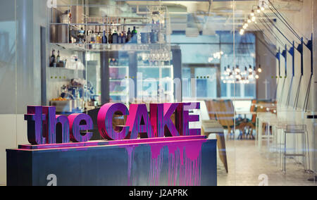 Cafe in einem modernen Stil mit einem violetten Inschrift machte den Kuchen von 3D Buchstaben auf dem dunklen Stand auf dem unscharfen Hintergrund der Bar. Es gibt auch cha Stockfoto