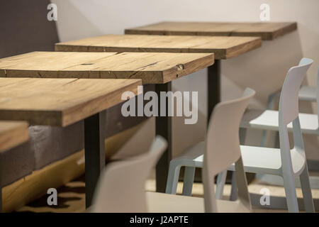 Quadratischen Holztischen mit schwarzen Beinen auf die Lichtwand Hintergrund. Neben ihnen gibt es Stühle und ein Sofa. Nahaufnahme Foto. Horizontale. Stockfoto