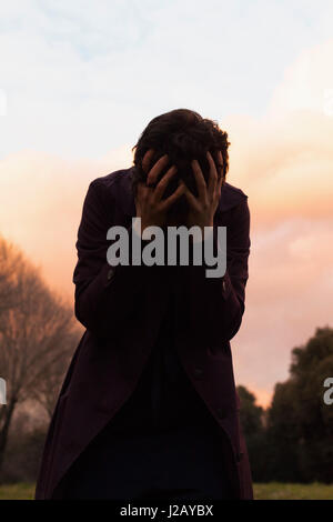 Depressive Frau mit Kopf in Händen gegen Himmel bei Sonnenuntergang Stockfoto