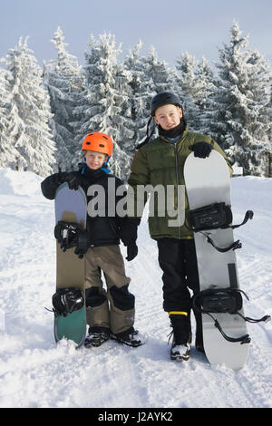 Voller Länge Porträt der Brüder mit snowboards auf Schnee gegen Bäume stehen Stockfoto