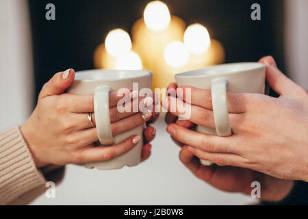 Bild des Paares mit Kaffeetassen gegen beleuchtete Kerzen zu Hause abgeschnitten Stockfoto