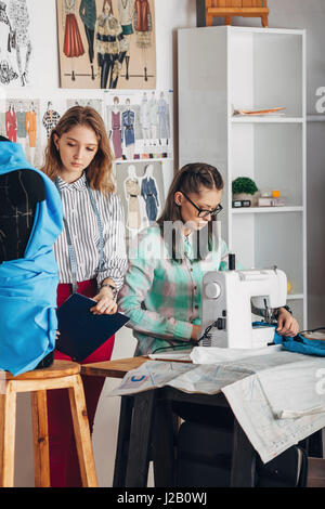 Schöne Assistentin durch weibliche Designer arbeiten an der Nähmaschine im Studio stehen Stockfoto