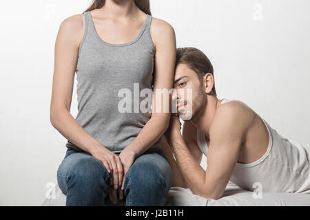 Nachdenklicher Mann stützte sich auf Freundin sitzen am Bett vor weißem Hintergrund Stockfoto
