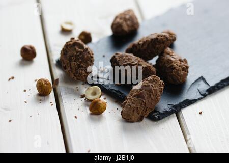 Schokolade Trüffel Pralinen mit Milch Schokolade Späne bedeckt und dekoriert von Haselnuss Kerne auf Schiefer mit Board und weißer Holztisch Stockfoto