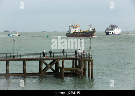 Gruppe von Männern, die von einem alten Anlegestelle in der Nähe der Ufermauer in alten Portsmouth Angeln. Es gibt viele Aktivität hinter mit Schiffe Fähren und ein Hovercraft. Stockfoto