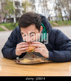 Mann isst sehr leckeren Burger in Suppen café Stockfoto