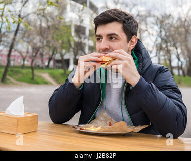 Ein junger Mann beißt ein Burger in einer Snack-Bar. Stockfoto