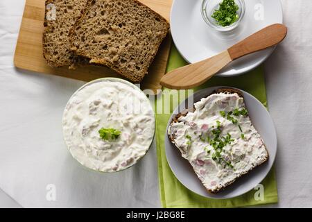 Scheibe Roggen-Vollkornbrot mit zarten hellen und frischen Quark Ausbreitung mit Schnittlauch und Petersilie bestreut. Verbreitung von Messer und einige e Holz Stockfoto